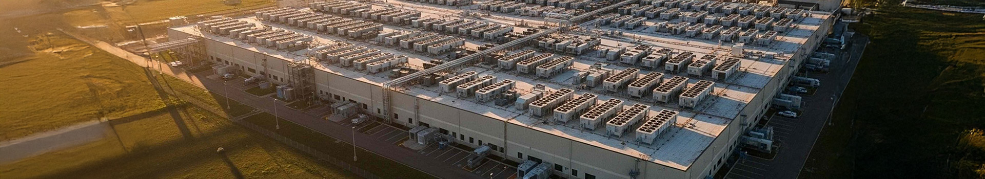 Aerial view of a large data center complex with extensive rooftop cooling units at sunset