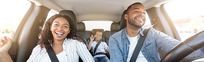 Happy family of three enjoying a car ride, with parents smiling in the front seats and a child smiling in the back seat.