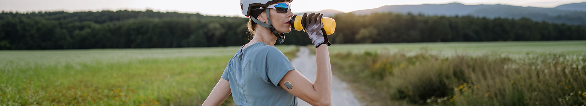 Diabetic cyclist with a continuous glucose monitor on her arm drinking water during her bike tour. 