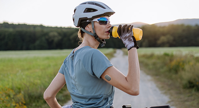 Diabetic cyclist with a continuous glucose monitor on her arm drinking water during her bike tour. 