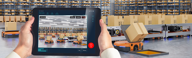 Person using tablet to monitor automated warehouse robots sorting packages via smart vision system