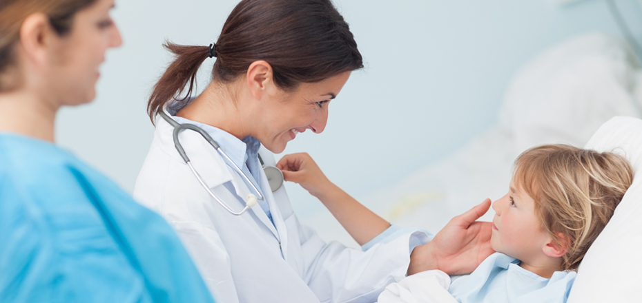 Female doctor and nurse smiling while comforting child patient in hospital bed.