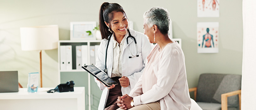 Doctor in white coat shows tablet to smiling older patient.