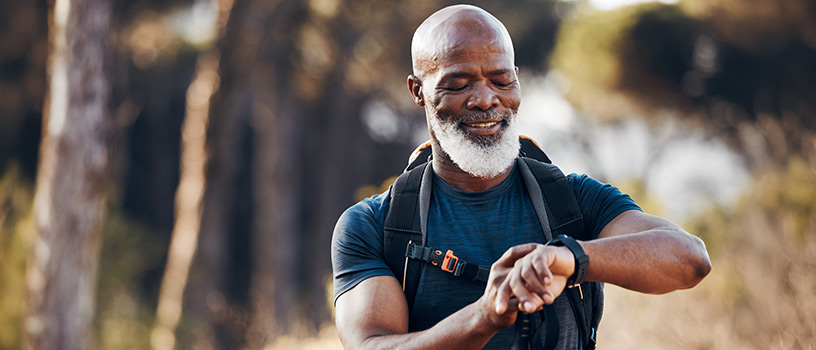 Smiling older Black man checking smartwatch while hiking.