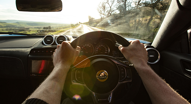 Lotus car interior and a person holding sterring wheel driving on a country road