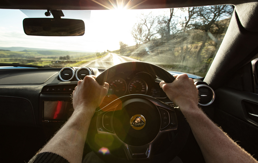 Lotus car interior and a person holding sterring wheel driving on a country road