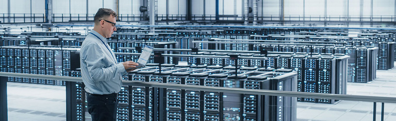 Man with laptop in a large data center with glowing servers.
