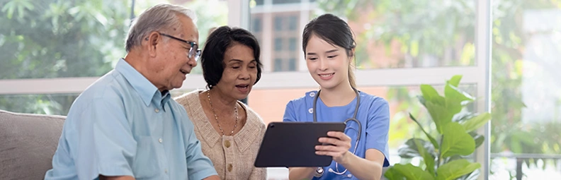Nurse shows tablet to smiling elderly couple.