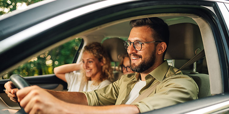 Smiling man in glasses driving car with family.