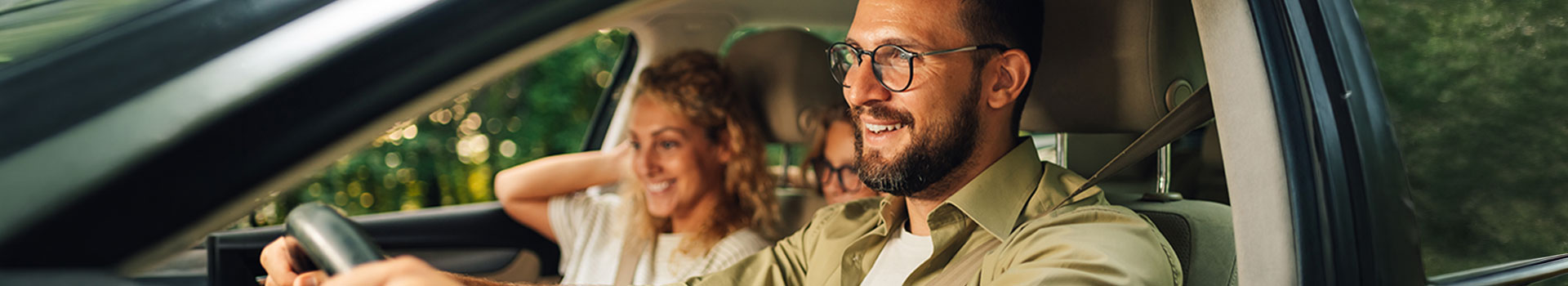 Smiling man in glasses driving car with family.