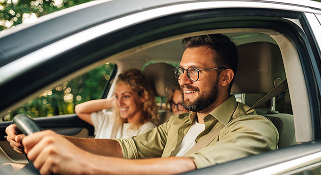 Smiling man in glasses driving car with family.