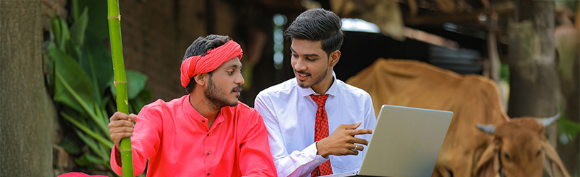 Young professional using laptop to explain technology to farmer in rural setting