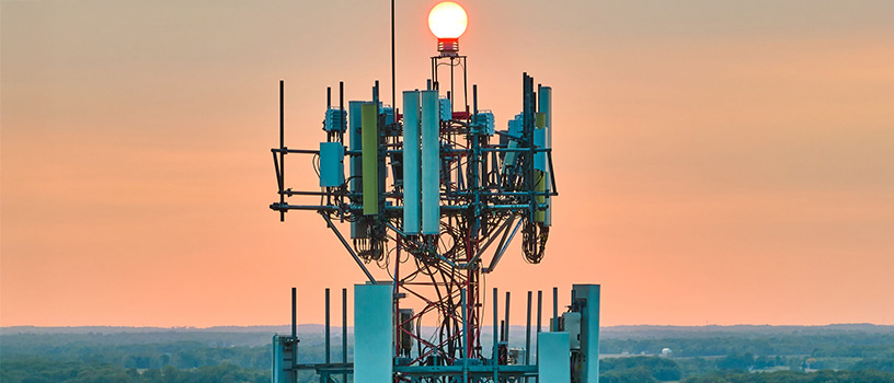 Close-up of cellular communication tower antennas against an orange sky at sunset