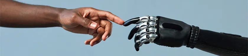 Human finger with dark skin touching a metallic robot finger.
