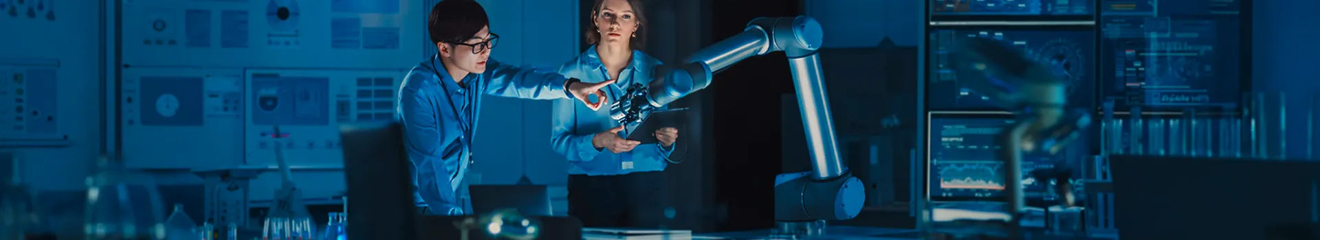 Two engineers collaborate with a robotic arm in a blue-lit lab.