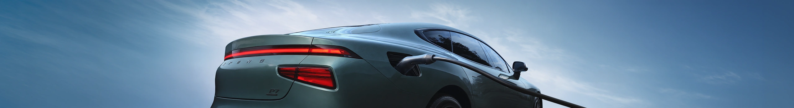 Teal electric car charging under a bright blue sky.