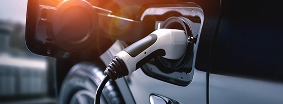 White EV charging cable plugged into a dark car.