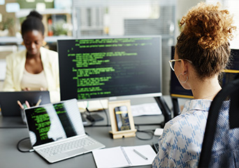 Female software developer writing code on a computer monitor in a modern office setting.