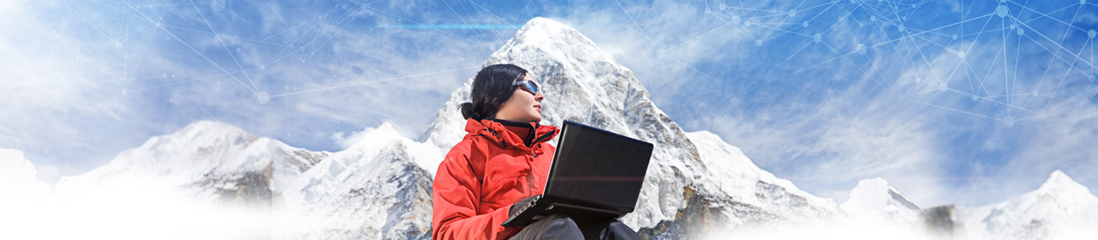 Woman seated with Laptop computer on lap seated at the base of a snow covered mountain.