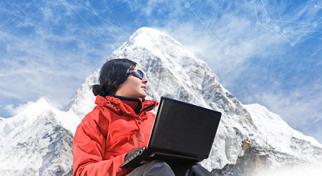 Woman seated with Laptop computer on lap seated at the base of a snow covered mountain.