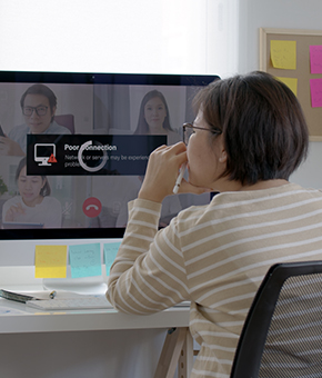 Image shows a female student at a desk look at a remote classroom video meeting on a computer while the conference has poor connection on the screen.