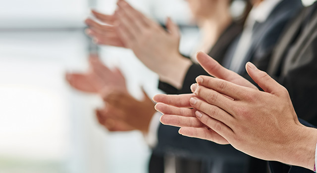 Close-up of business professionals clapping in appreciation, dressed in formal attire, symbolizing recognition and achievement.