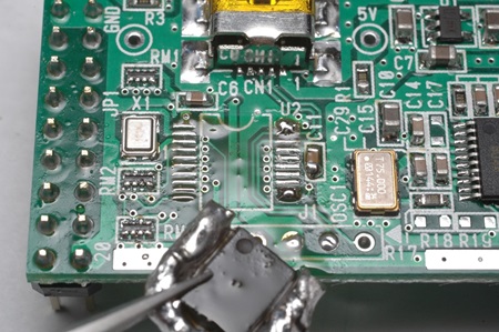 電子基板からピンセットを使用したICチップの取り外し作業の様子。ピンセットでICチップを掴み、ハンダが溶けた状態で慎重に持ち上げている場面です。SOP部品の取り外し手順の最終ステップを示す技術写真で、正しい取り外し方法とパッド損傷防止のポイントを視覚的に解説しています。