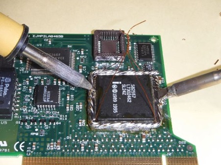 QFP品取り外し作業における2本のハンダごてを使用した同時加熱の様子。緑色の電子基板上のQFPチップの対向する2辺に2本のハンダごてが当てられ、銅線を介してハンダを溶かしている場面です。高度な電子部品修理技術を示す重要なステップで、均等な加熱によりQFPチップの全ピンのハンダを同時に溶かす専門的な手法を視覚的に解説しています。